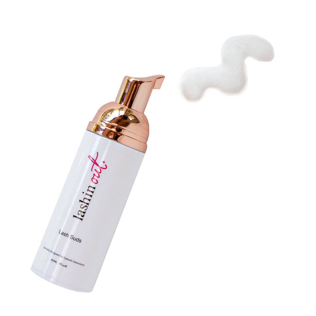 A bottle of lash suds with a small amount of foam shown. The bottle is white and the pump top is gold.
