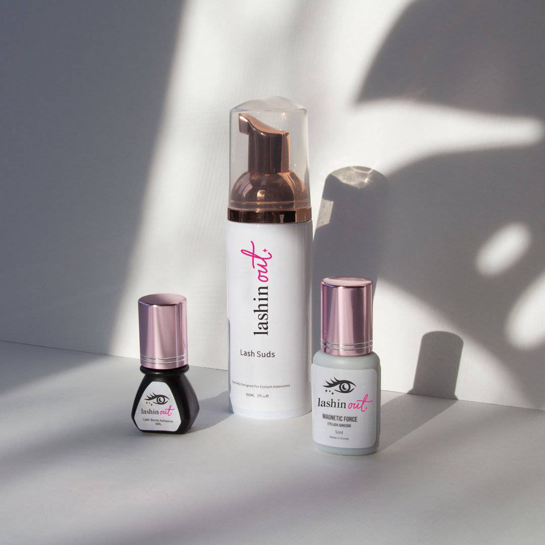 3 bottles are shown. The first bottle is a lash adhesive. The bottle is black with a pink top. The second bottle is Lash Suds. The third bottle is Out of Sight clear lash adhesive.