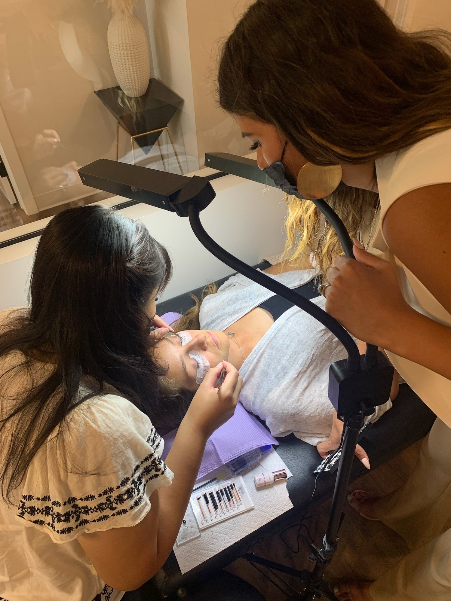 A student is applying eyelash extensions to a model and the teacher is watching her work. 