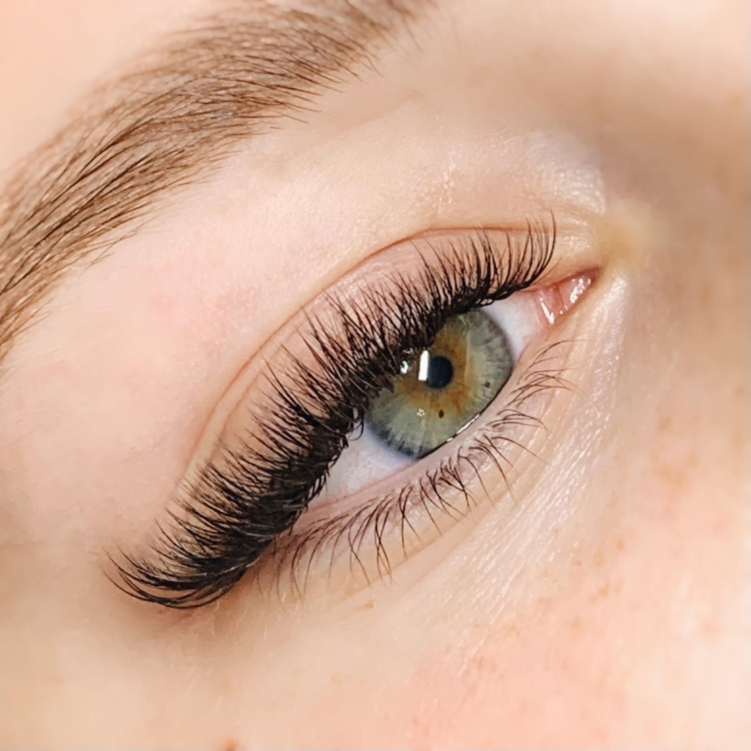 Hybrid eyelash extensions on a woman with blue eyes. The eyelashes are full and of varying lengths.The photo shows very good technique, with no big gaps, clumps, or stickies.  