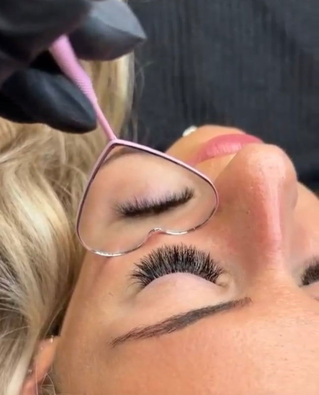 Lash technician using an under-eye mirror to confirm the client’s eyes are fully closed during eyelash extension application.