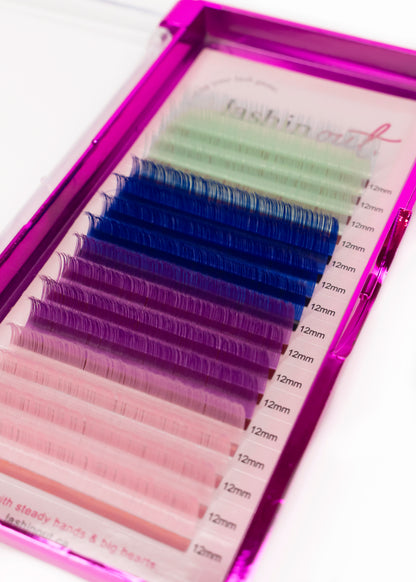 A tray of multicolored lashes. The colors are white, dark blue, purple and light pink. There are four lines of each color. They are 12 mm lashes. 