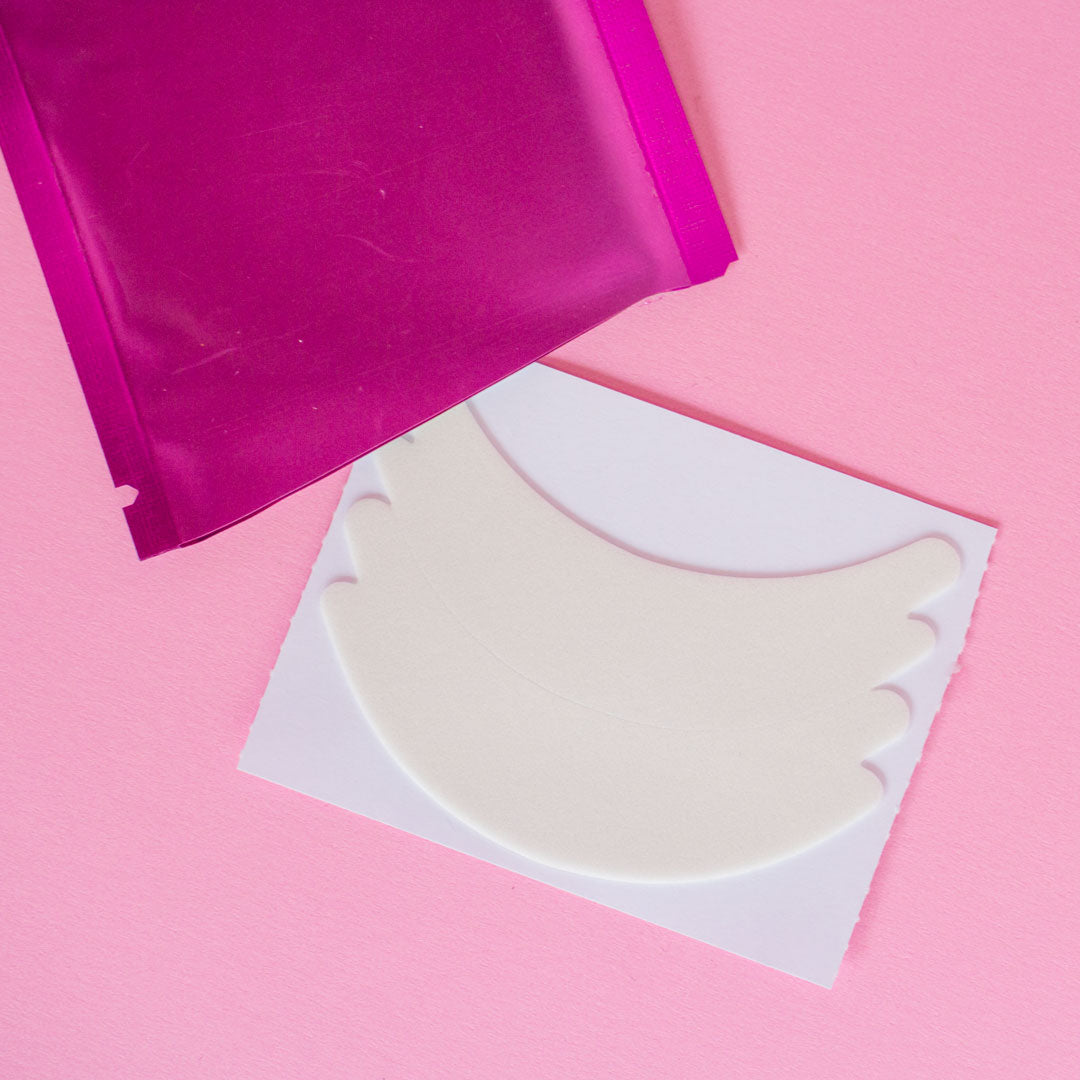 An opened package of flexi Foam Eye Pads. The package is pink and empty with the foam eye pads on the table beside the empty package. 