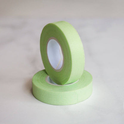 Two rolls of green lash tape. One is laying down and the other one is upright sitting in the center of the bottom roll. 